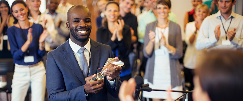 Man holding award trophy with audience clapping behind him.