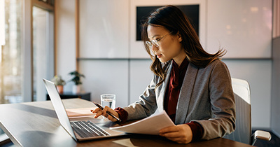 Woman typing on computer and holding documents.