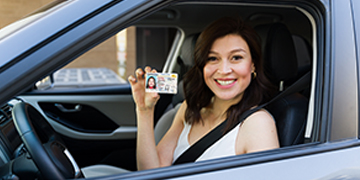 Woman in car holding up California driver's license.