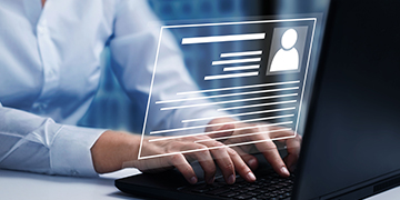 Person typing on a laptop with a digital profile holographically displayed above the keyboard.